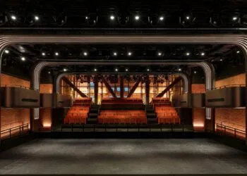 Apple Music Hall in Battersea Power Station: view across the open floor to red seating tiers, balconies and brick walls, with a glass wall behind
