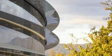 Curved glass facade of Apple Park with several canopies in front of trees and hills – Apple's headquarters, whose services business Bank of America sees at risk from AI agents