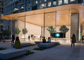 Apple Store Genius Bar: exterior view of an Apple Store with a glass front, wooden canopy and a plaza with stone benches at dusk