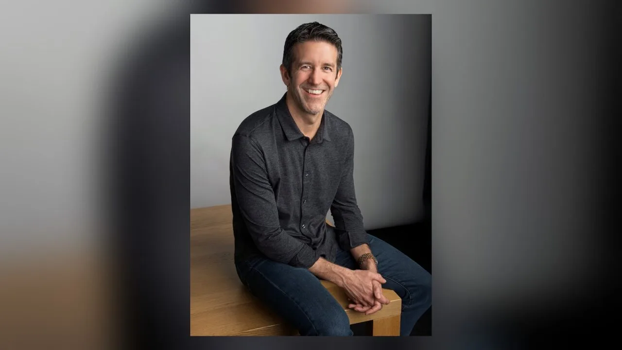 Thanksgiving week off at Apple: CEO John Ternus in a dark shirt sitting on a wooden table, smiling
