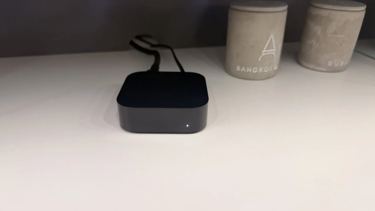 Apple TV 4K A19: black Apple TV box with glowing status light on a light shelf
