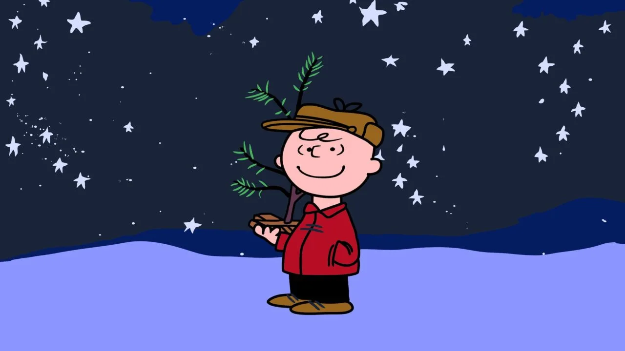 Charlie Brown holding a small Christmas tree under a starry sky in the snow, a scene from A Charlie Brown Christmas, free again on Apple TV