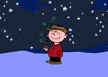 Charlie Brown holding a small Christmas tree under a starry sky in the snow, a scene from A Charlie Brown Christmas, free again on Apple TV