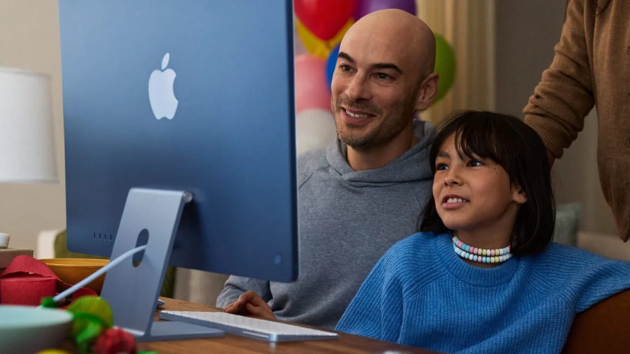 A child sits with an adult in front of a blue iMac, image for Apple's guide on family screen time