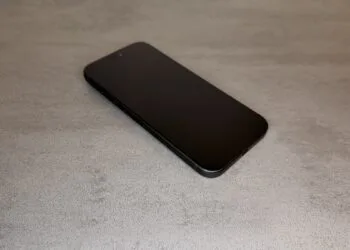 iPhone 20 display comparison: current black iPhone Pro with a flat display, shown at an angle from above on a grey stone surface
