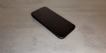 iPhone 20 display comparison: current black iPhone Pro with a flat display, shown at an angle from above on a grey stone surface