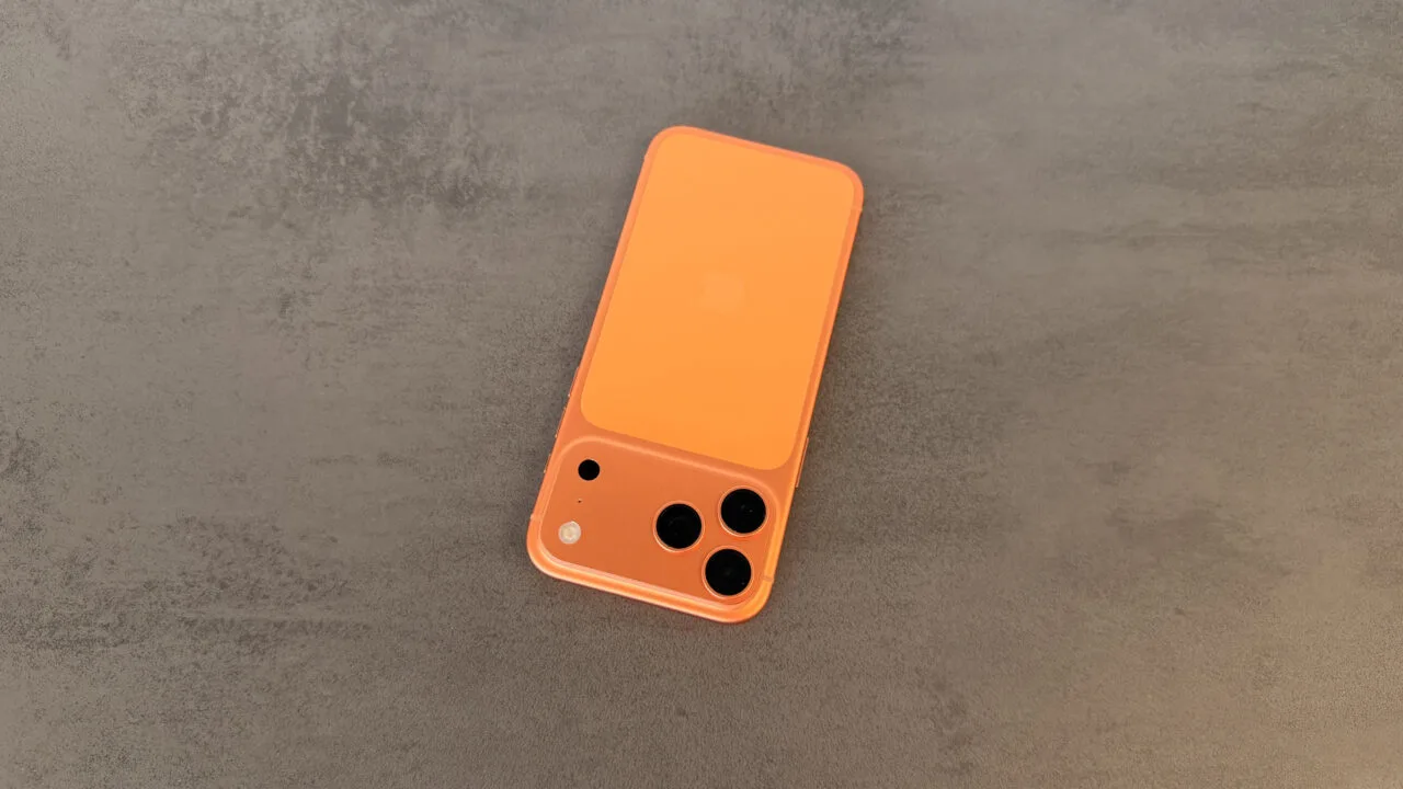 Orange iPhone with a triple camera lying on grey stone, illustrating the increase in iPhone production