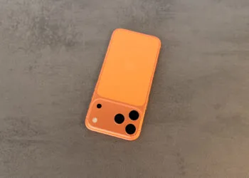 Orange iPhone with a triple camera lying on grey stone, illustrating the increase in iPhone production
