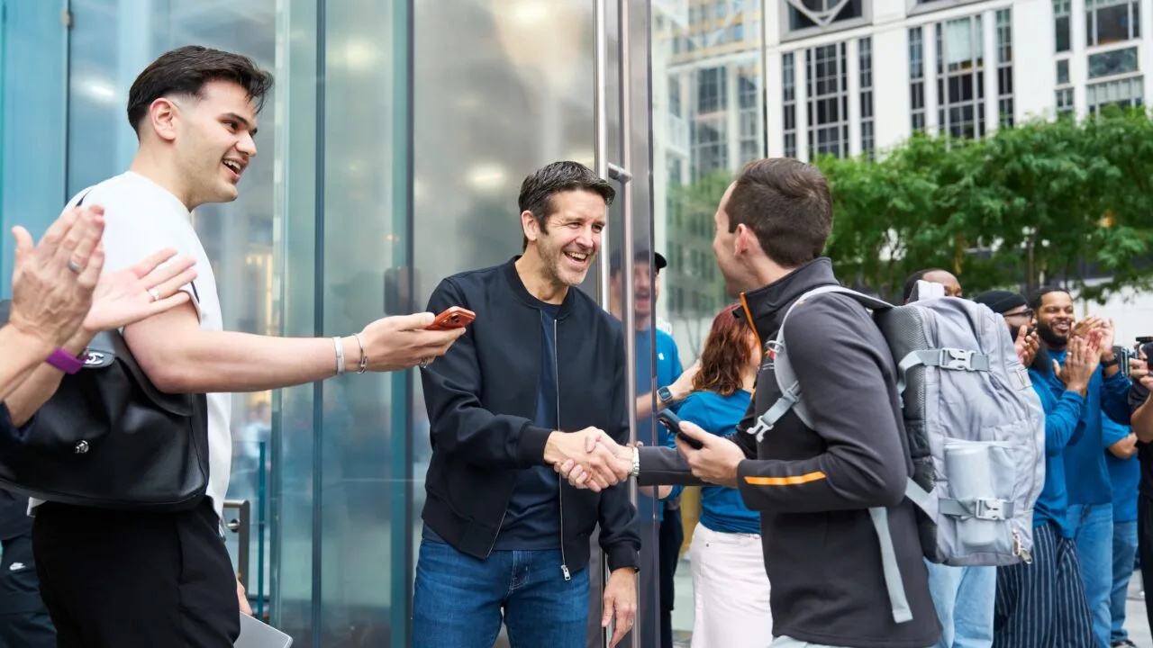 John Ternus shakes hands with a customer outside Apple Fifth Avenue in New York, surrounded by applauding employees