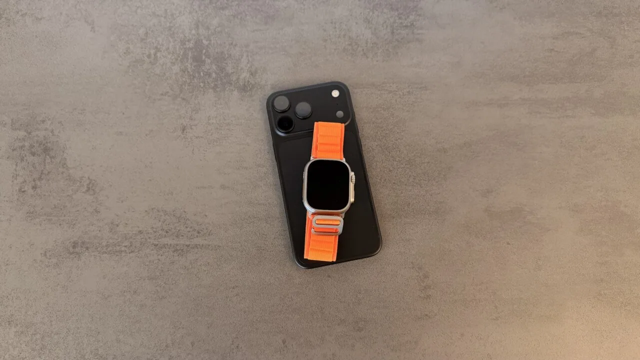 Taptic Engine in iPhone and Apple Watch: black iPhone with triple camera and an Apple Watch Ultra with an orange Alpine Loop on top