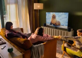 Apple Event Welcome home: a family in a living room watching TV with Apple TV, two HomePod speakers beside the screen and two green HomePod mini speakers behind the sofa