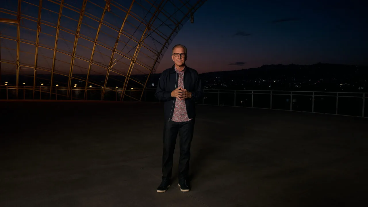 Greg Joswiak, Apple's head of marketing, stands at dusk on a terrace beneath a curved steel and glass structure