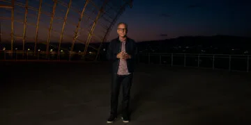 Greg Joswiak, Apple's head of marketing, stands at dusk on a terrace beneath a curved steel and glass structure