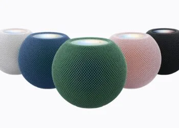 HomePod mini 2 in white, blue, green, pink and midnight arranged in a semicircle, the green model in front with its top lit up
