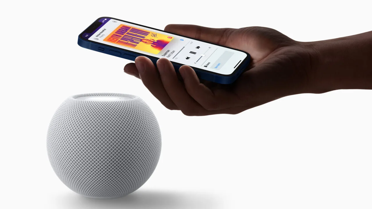 HomePod mini Siri AI: white HomePod mini with a hand above it holding an iPhone that shows music playback on the speaker