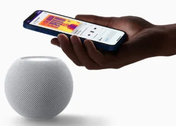 HomePod mini Siri AI: white HomePod mini with a hand above it holding an iPhone that shows music playback on the speaker
