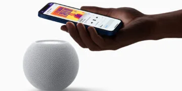 HomePod mini Siri AI: white HomePod mini with a hand above it holding an iPhone that shows music playback on the speaker