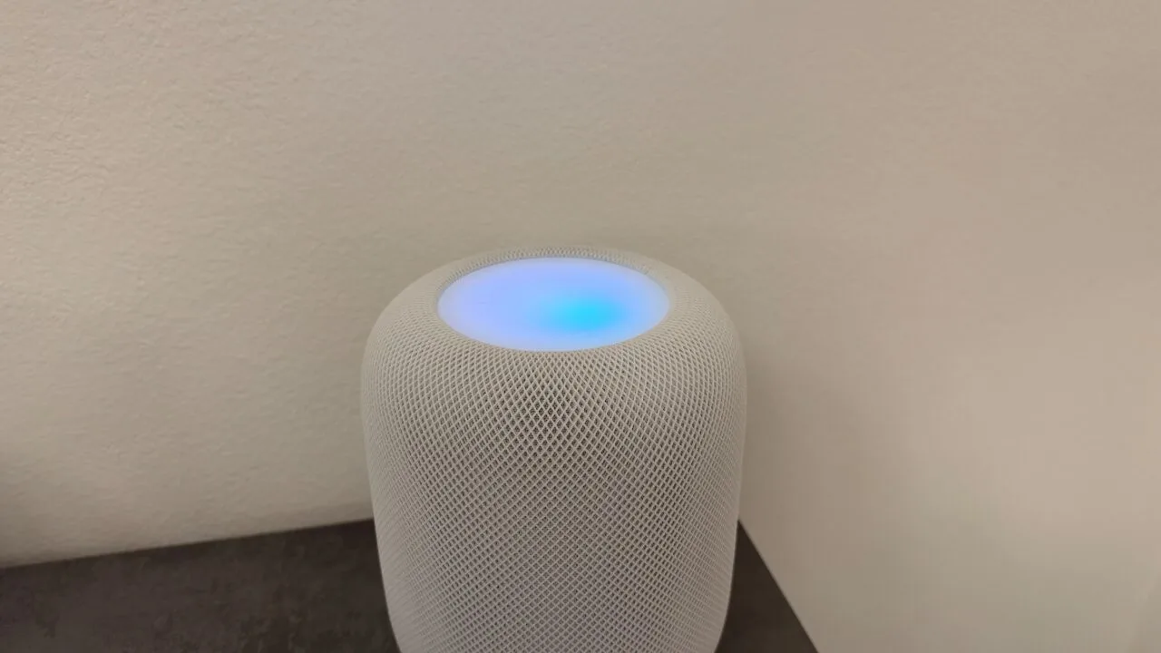 White HomePod with its top glowing in shades of blue and violet in front of a light wall – this is what HomePod Sound Glow looks like