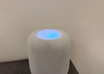 White HomePod with its top glowing in shades of blue and violet in front of a light wall – this is what HomePod Sound Glow looks like