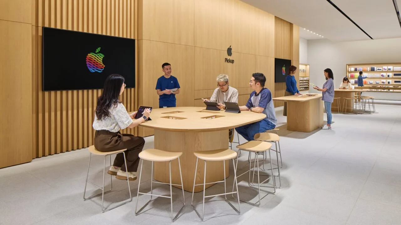 Symbolic image for iPhone China: Apple Store with wooden walls, customers working on iPads at a table next to a staff member