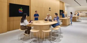 Symbolic image for iPhone China: Apple Store with wooden walls, customers working on iPads at a table next to a staff member