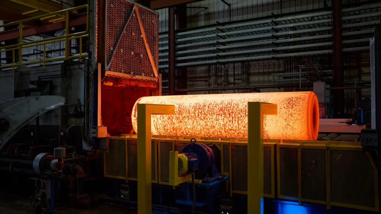 iPhone Duo titanium USA: glowing metal billet after leaving an industrial furnace in a factory hall, with yellow supports in front