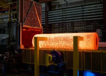 iPhone Duo titanium USA: glowing metal billet after leaving an industrial furnace in a factory hall, with yellow supports in front