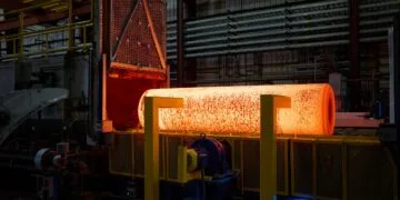iPhone Duo titanium USA: glowing metal billet after leaving an industrial furnace in a factory hall, with yellow supports in front