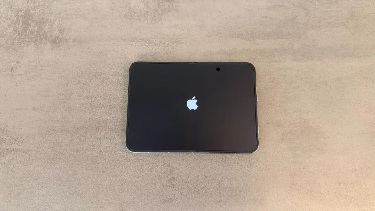 iPhone Duo recall: unfolded iPhone Duo lying flat on a grey table, the inner display showing the Apple logo during startup