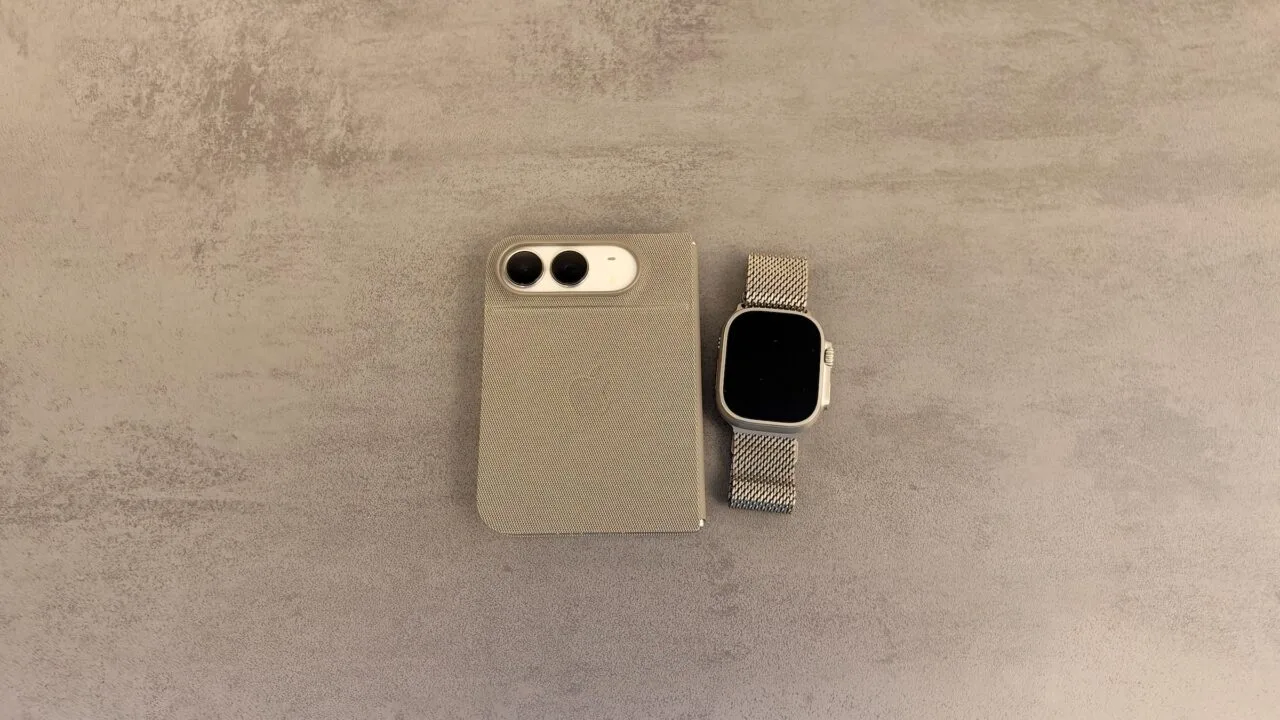 Unlocking iPhone Duo with Apple Watch: folded iPhone Duo in a case, camera side up, next to an Apple Watch Ultra with a mesh band on a grey stone surface