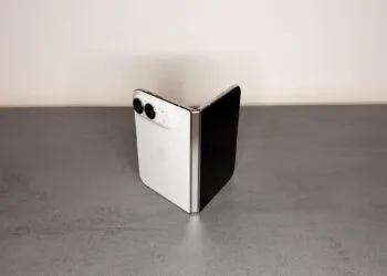 iPhone Duo hinge: a white iPhone Duo half unfolded and standing like a book on a gray stone surface, with the silver hinge facing the camera