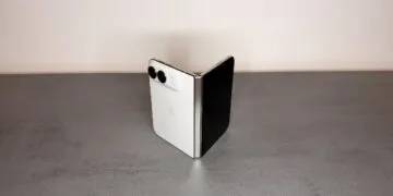 iPhone Duo hinge: a white iPhone Duo half unfolded and standing like a book on a gray stone surface, with the silver hinge facing the camera