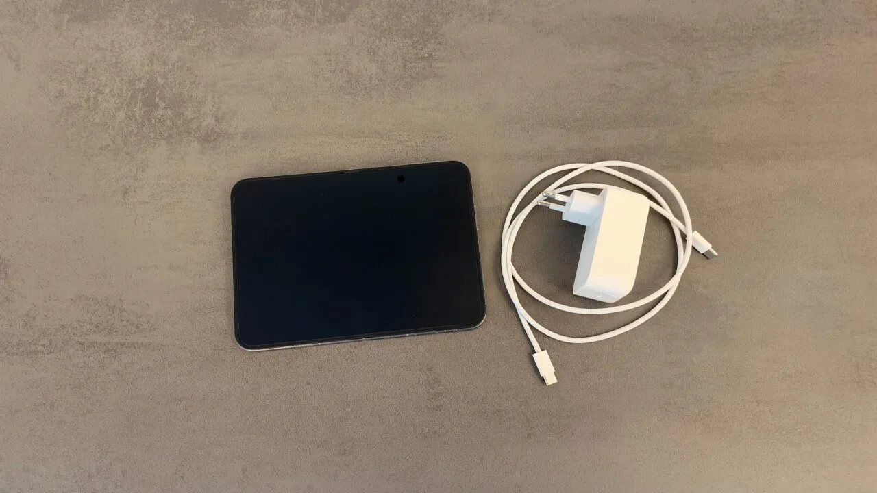 iPhone Duo fast charging: an unfolded iPhone Duo on a gray stone surface next to a white USB-C power adapter and a braided USB-C charging cable