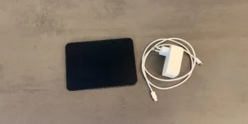 iPhone Duo fast charging: an unfolded iPhone Duo on a gray stone surface next to a white USB-C power adapter and a braided USB-C charging cable