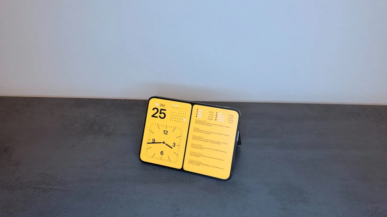 iPhone Duo StandBy on a kickstand: the fully unfolded iPhone Duo stands angled in landscape, showing the date, a calendar, a clock and stock prices.