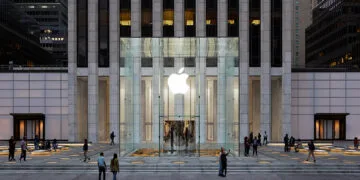 The Apple Store on Fifth Avenue in New York, set to receive more than 150 iPhone Duo demo units: the glass cube with its illuminated Apple logo in front of the tower at dusk