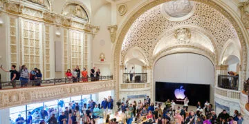 New Macs and iPad mini: visitors and camera crews inside Apple Tower Theatre in Los Angeles, with the stage and a glowing Apple logo behind them