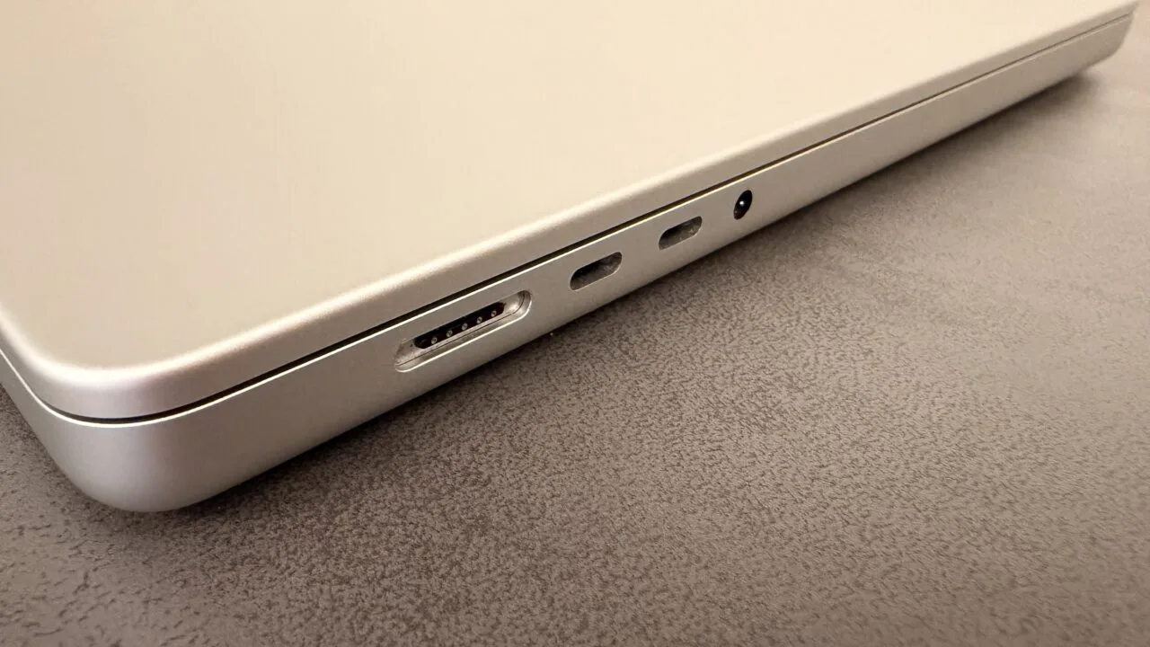 Silver MacBook on a dark tabletop showing the MagSafe port, two USB-C ports and the headphone jack, illustrating the 2027 notebook market
