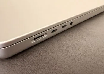 Silver MacBook on a dark tabletop showing the MagSafe port, two USB-C ports and the headphone jack, illustrating the 2027 notebook market