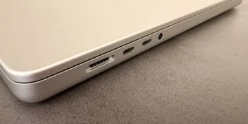 Silver MacBook on a dark tabletop showing the MagSafe port, two USB-C ports and the headphone jack, illustrating the 2027 notebook market