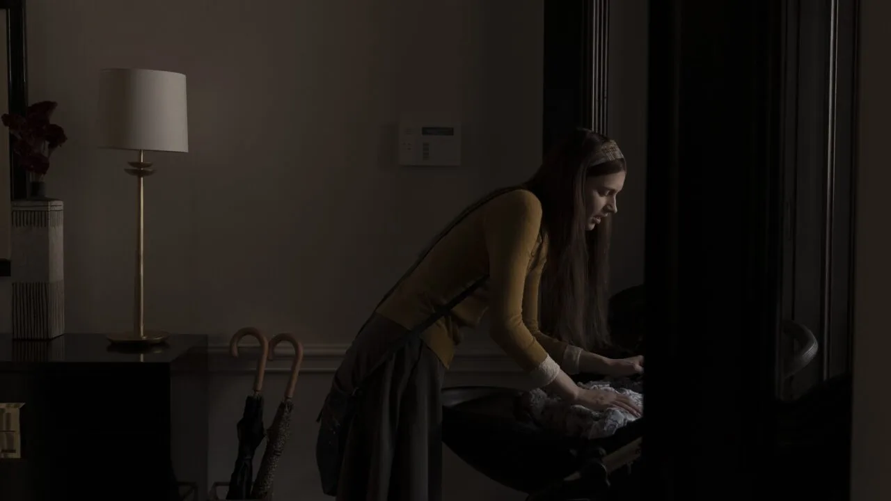 Scene from Servant: the nanny leans over a pram in a dark hallway, the series at the centre of the Apple lawsuit