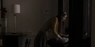 Scene from Servant: the nanny leans over a pram in a dark hallway, the series at the centre of the Apple lawsuit