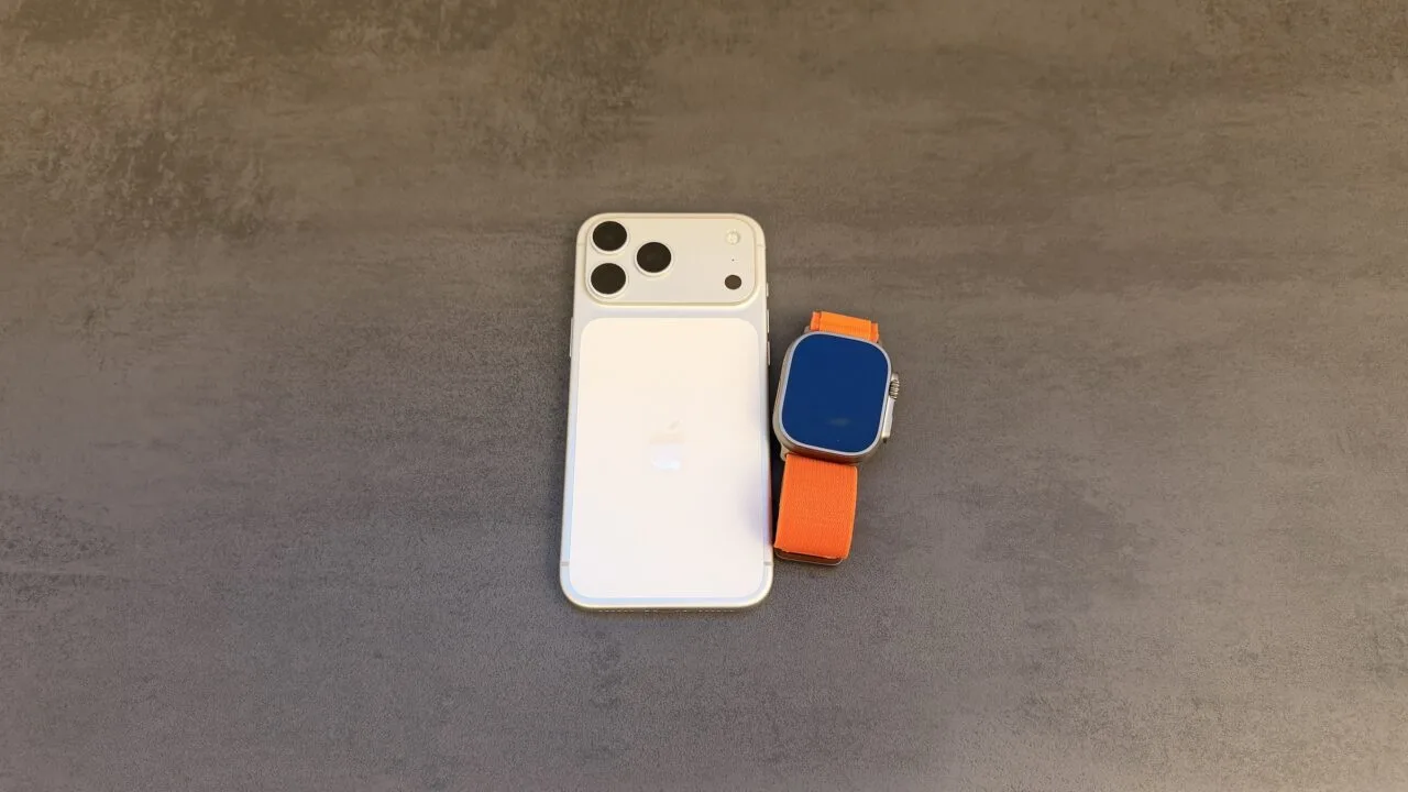 Taptic Engine patent dispute: white iPhone with triple camera seen from the back, next to an Apple Watch Ultra with an orange Alpine Loop on a grey surface