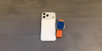 Taptic Engine patent dispute: white iPhone with triple camera seen from the back, next to an Apple Watch Ultra with an orange Alpine Loop on a grey surface