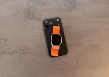 Taptic Engine royalties: black iPhone with camera plateau and an Apple Watch Ultra with an orange Alpine Loop on top, lying on a grey stone table